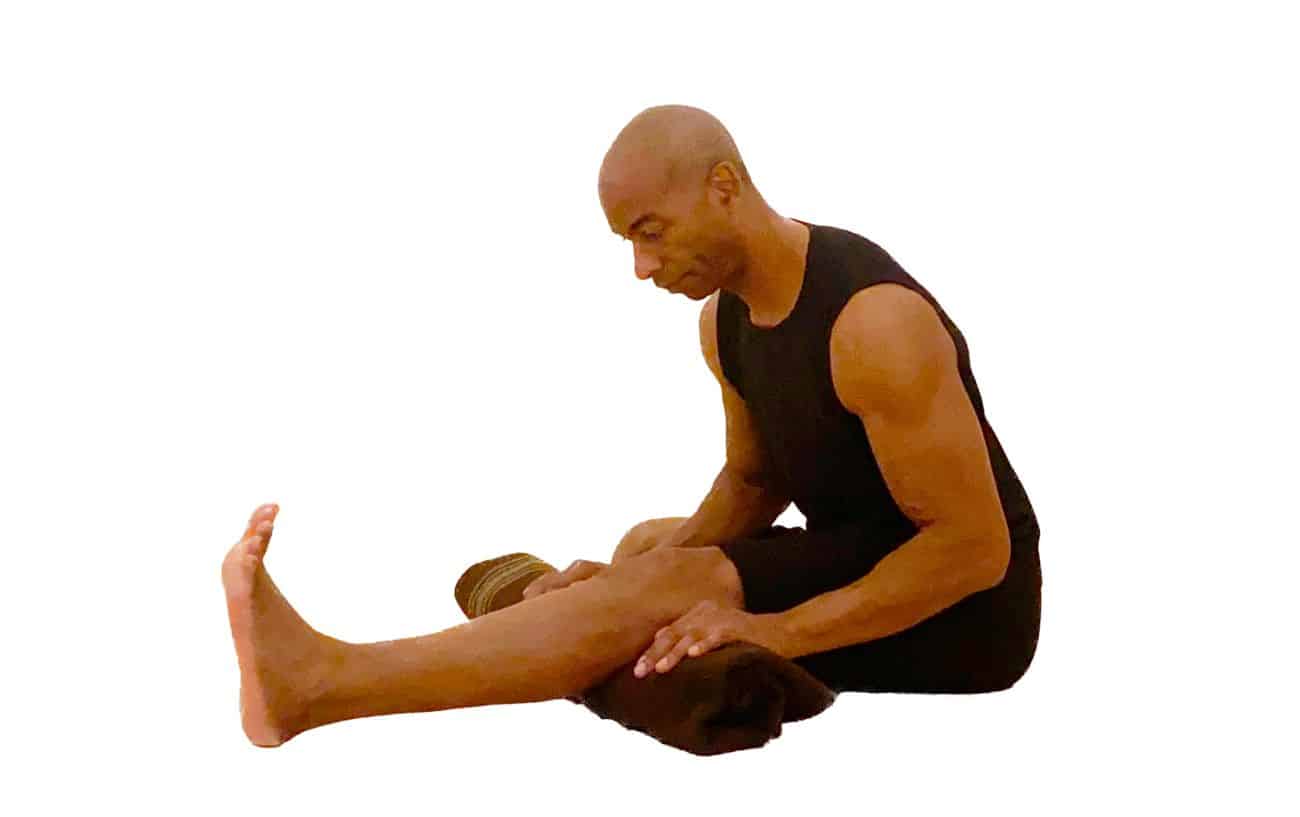 a man wearing black yoga clothes doing head to knee pose with a blanket under his knee