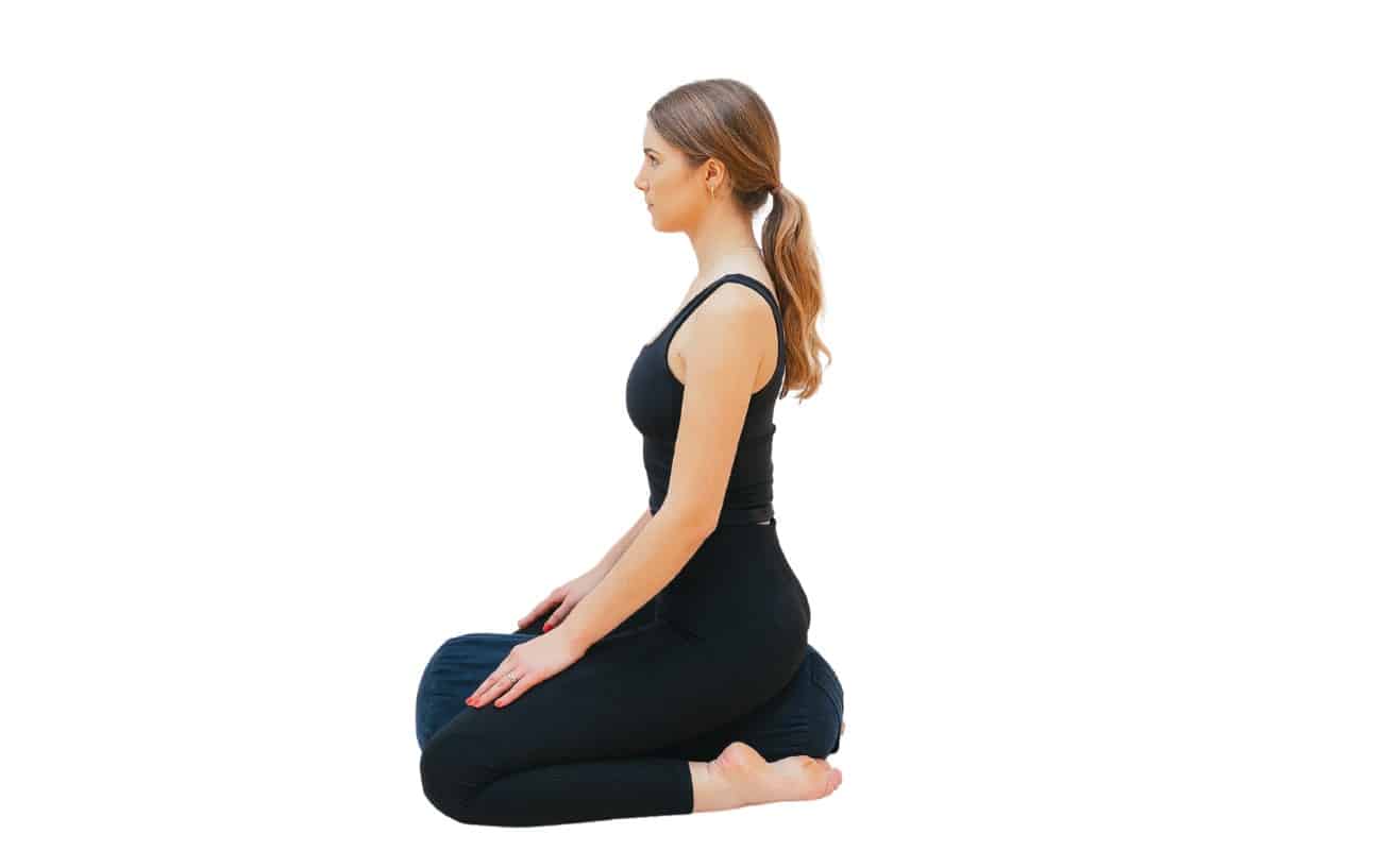 a woman doing hero pose with a bolster between her legs