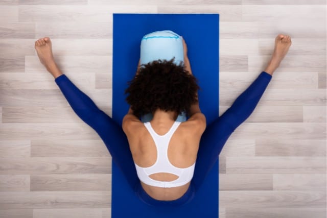 a woman doing a wide legged forward fold on a blue yoga mat