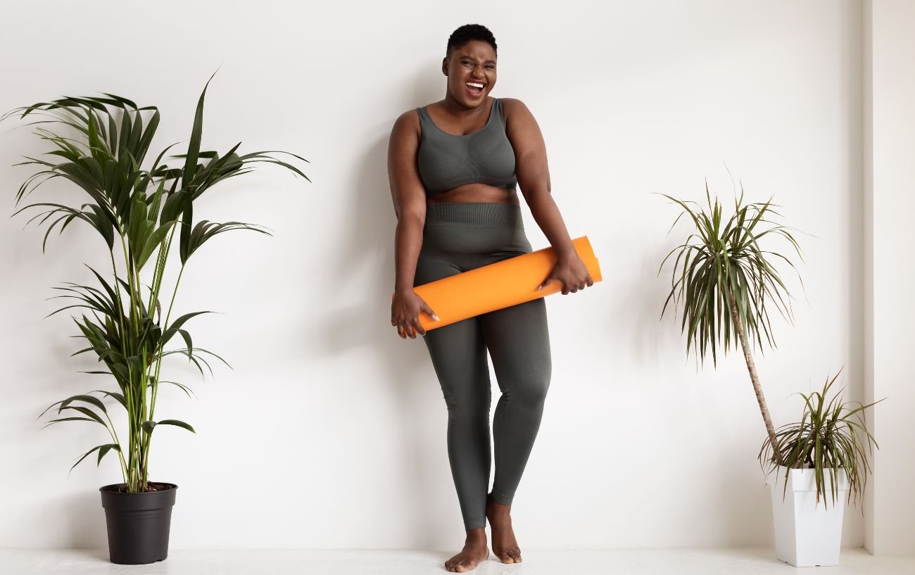 A woman holding an orange yoga mat and smiling.