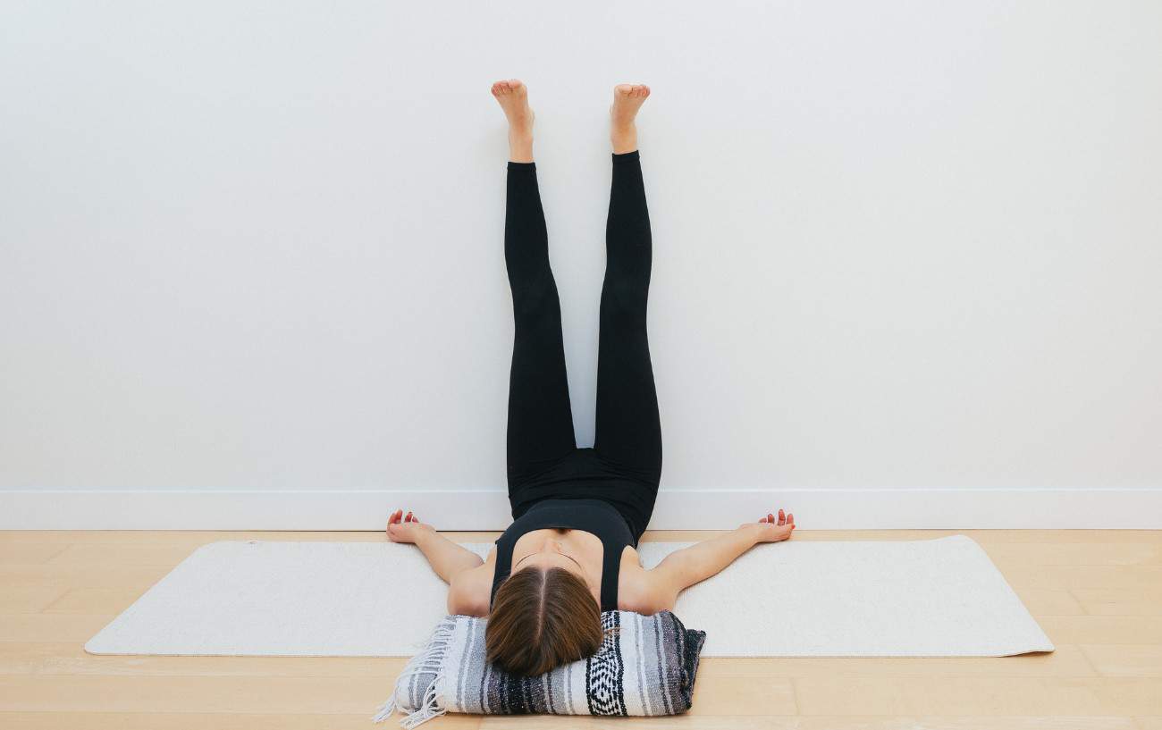 woman doing the legs up the wall pose in a yoga studio with a blanket under her head