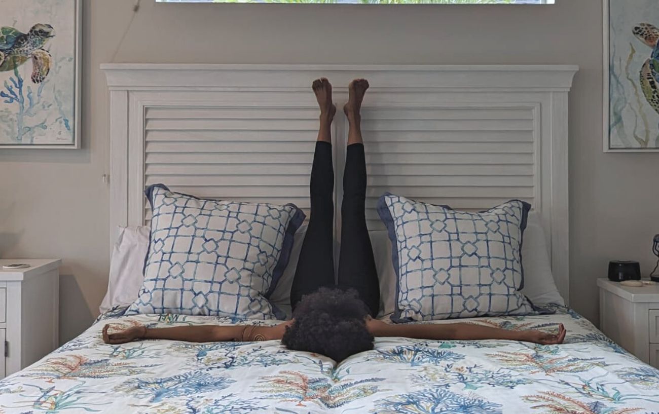 a woman doing legs up the wall pose in black yoga clothes in bed