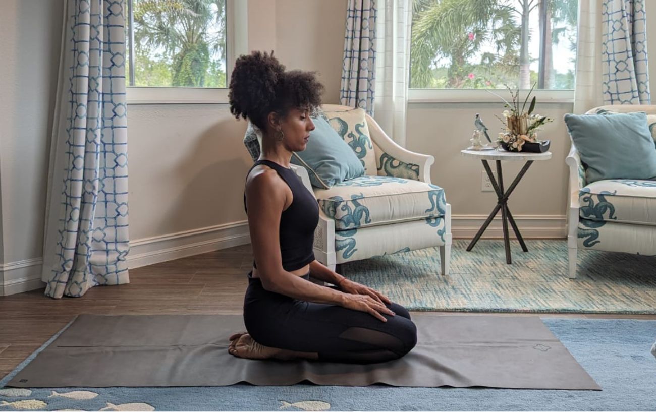 a woman wearing black yoga clothes doing yoga neck stretches kneeling in her living room