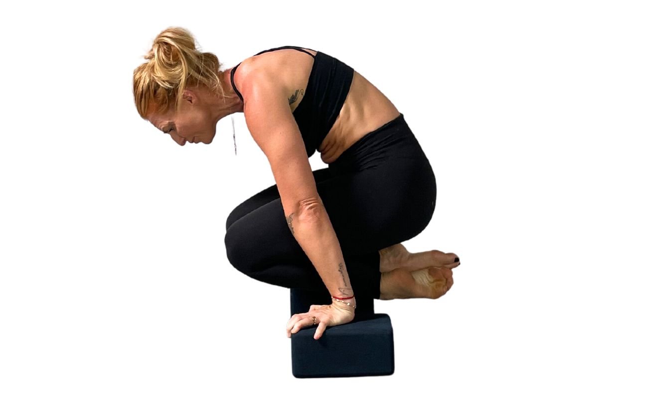 a woman wearing black yoga clothes doing lolasana on blocks