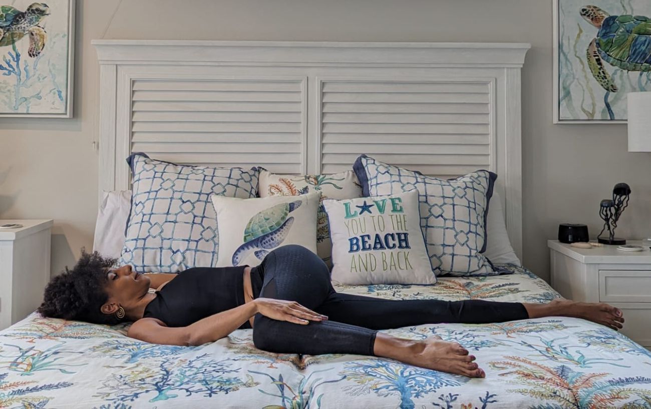 a woman doing lying down twisting pose in black yoga clothes in bed