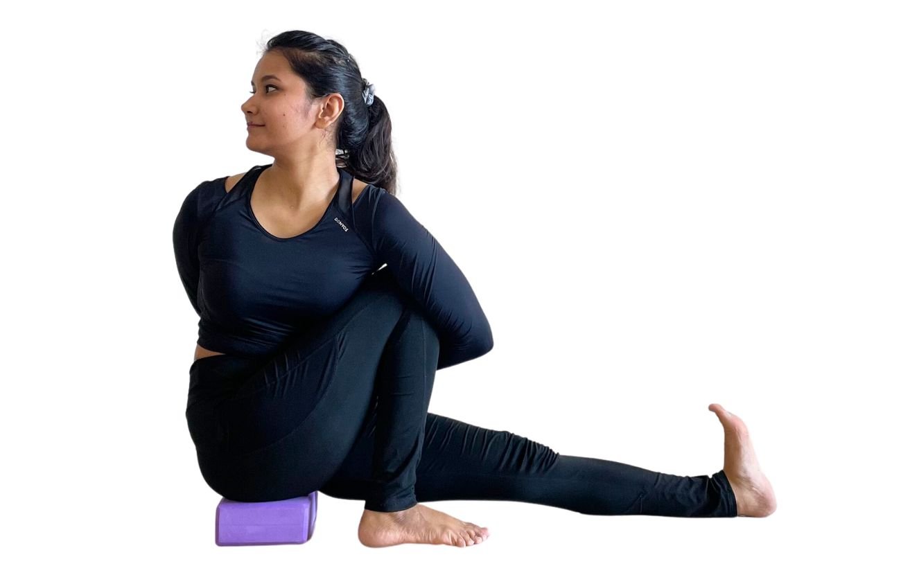 a woman wearing black yoga clothes doing Marichyasana C on a purple block