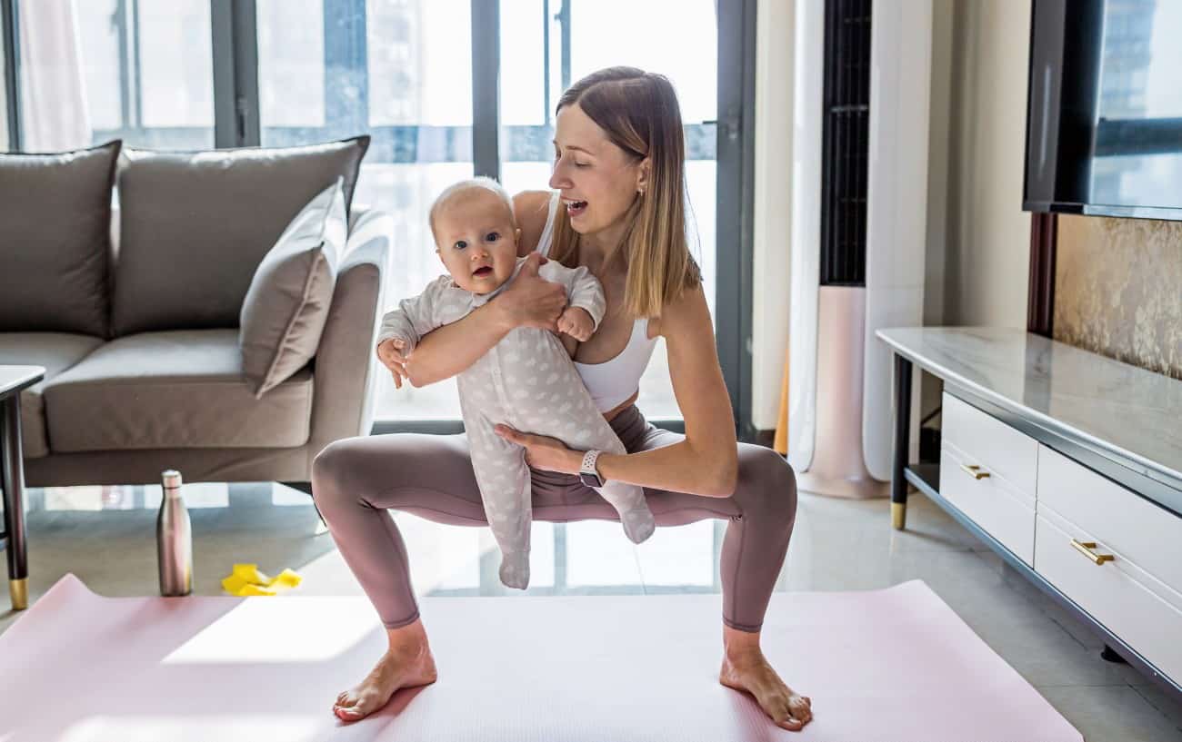 woman performs a yoga squat while holding a baby