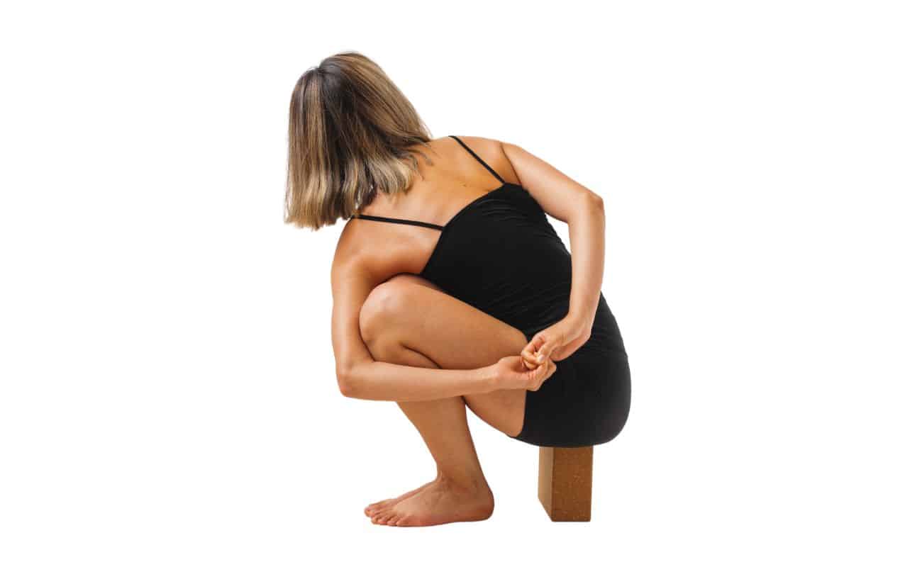 woman wearing black yoga clothes in noose pose on a yoga block