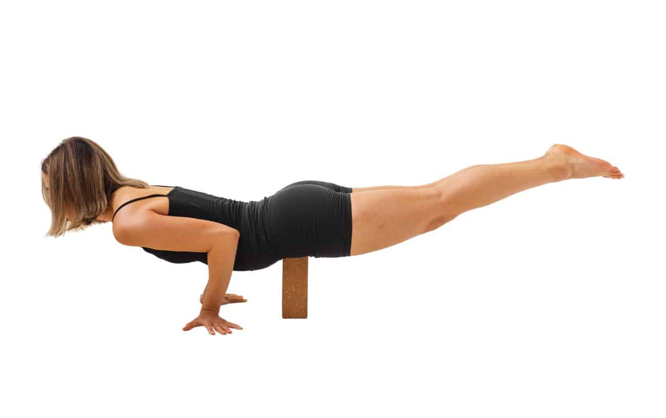 a woman wearing black yoga clothes in peacock pose using a block for support