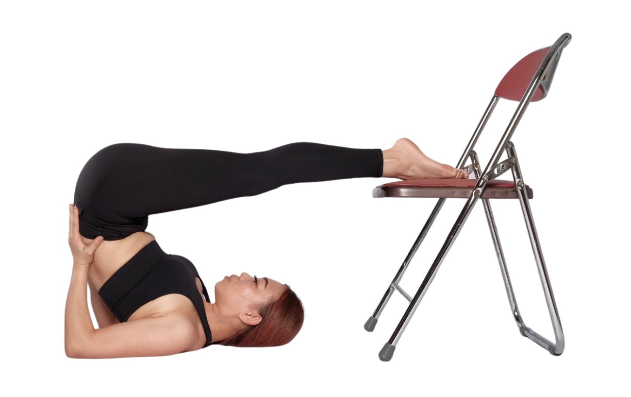 a woman wearing black yoga clothes in plow pose with her feet resting on a chair