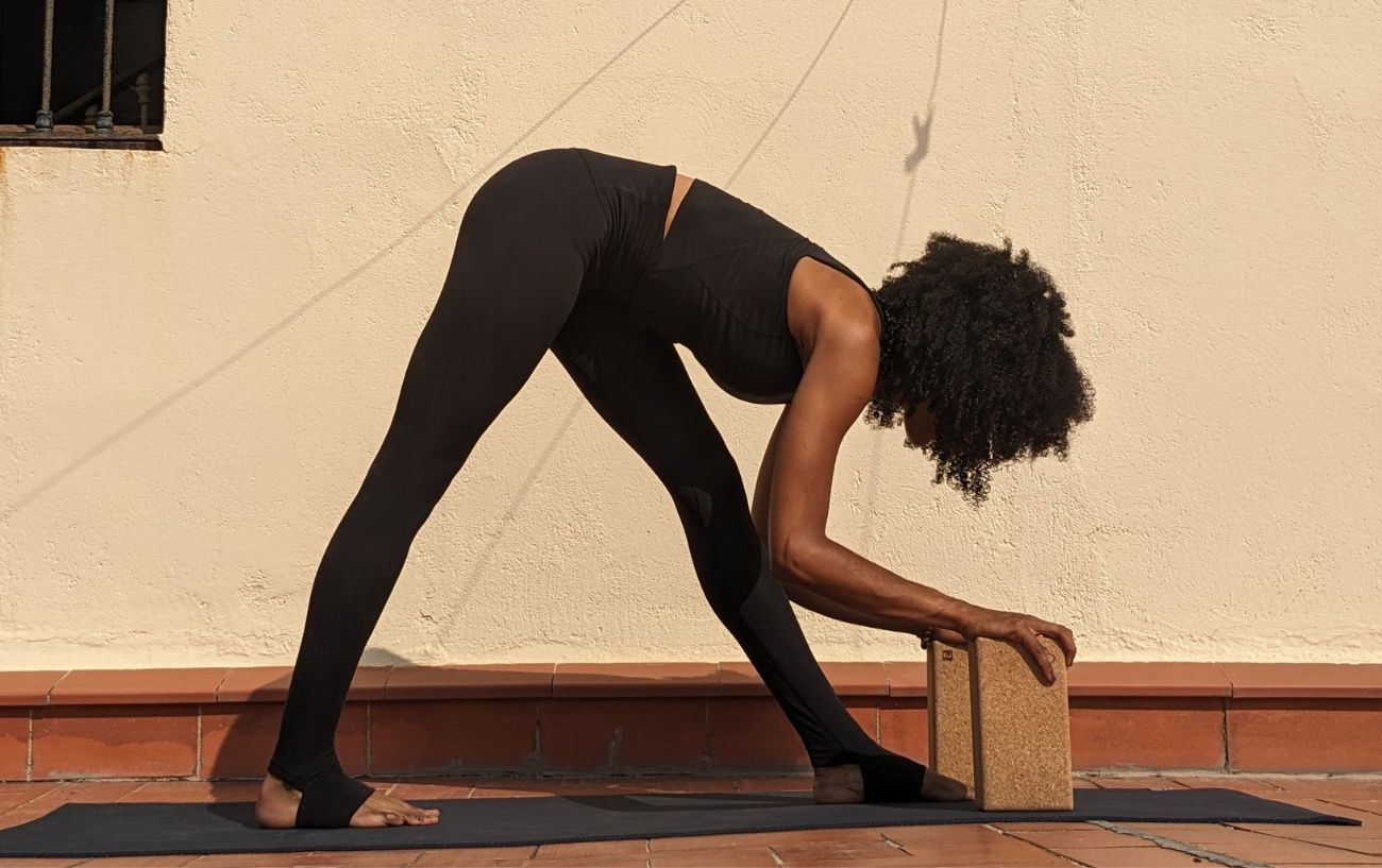 a woman wearing black yoga clothes doing pyramid pose on a sunny terrace