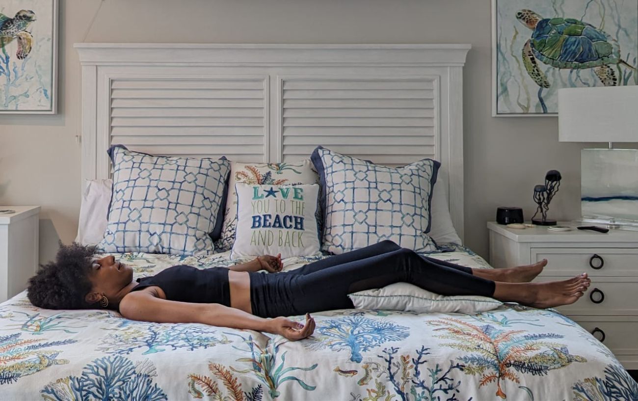 a woman doing savasana in black yoga clothes in bed