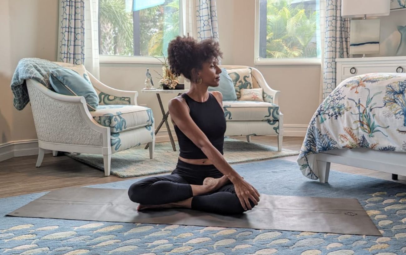 a woman doing a seated twist pose in black yoga clothes in a living room