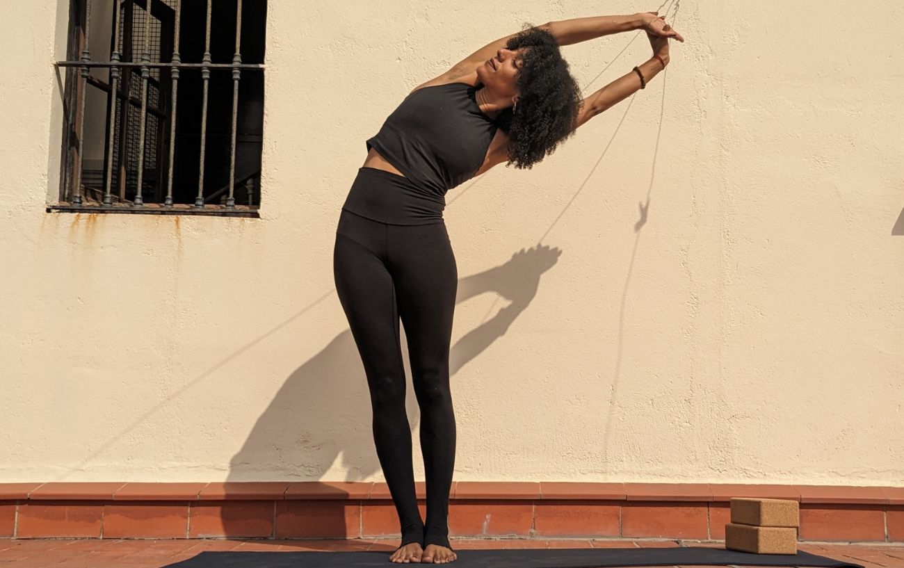 a woman wearing black yoga clothes doing standing side bend on a sunny terrace