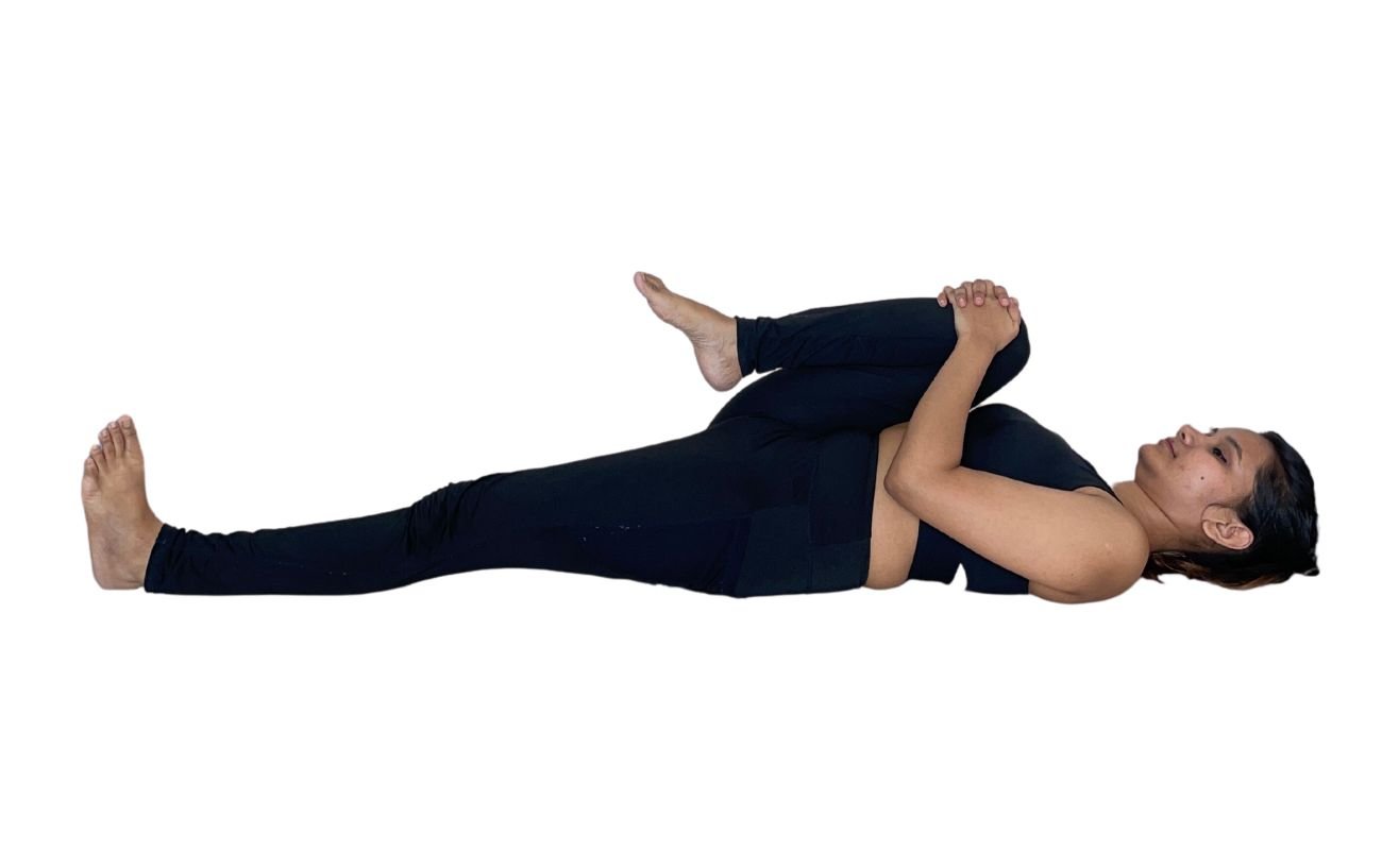 a woman in black yoga clothes doing single leg wind relieving pose