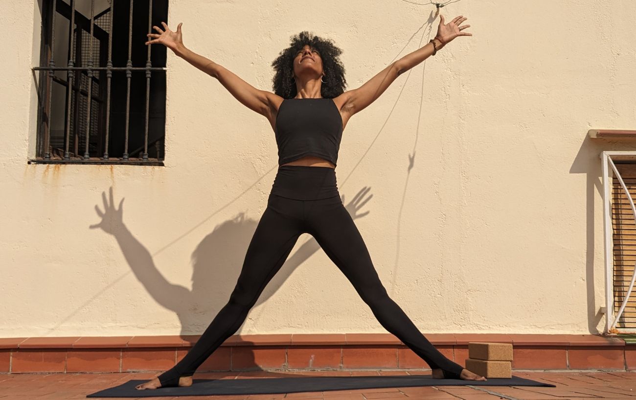 a woman wearing black yoga clothes doing five pointed star pose on a sunny terrace