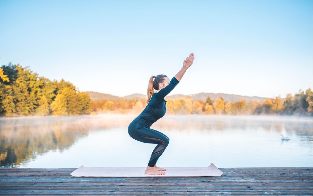 a woman doing a yoga chair pose in front of a lake