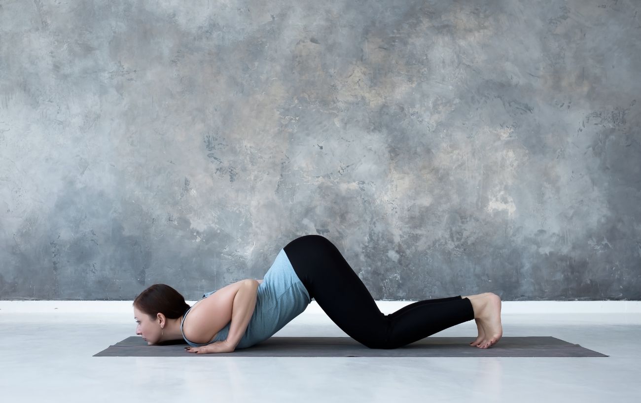 a woman doing sun salutation c, knees chest chin pose in a grey room