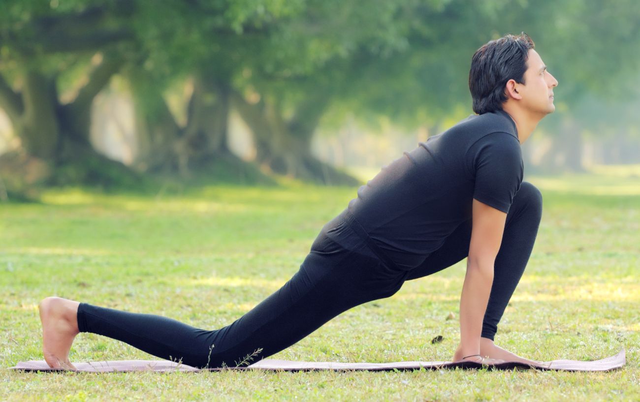 a man doing a low yoga lunge in a park