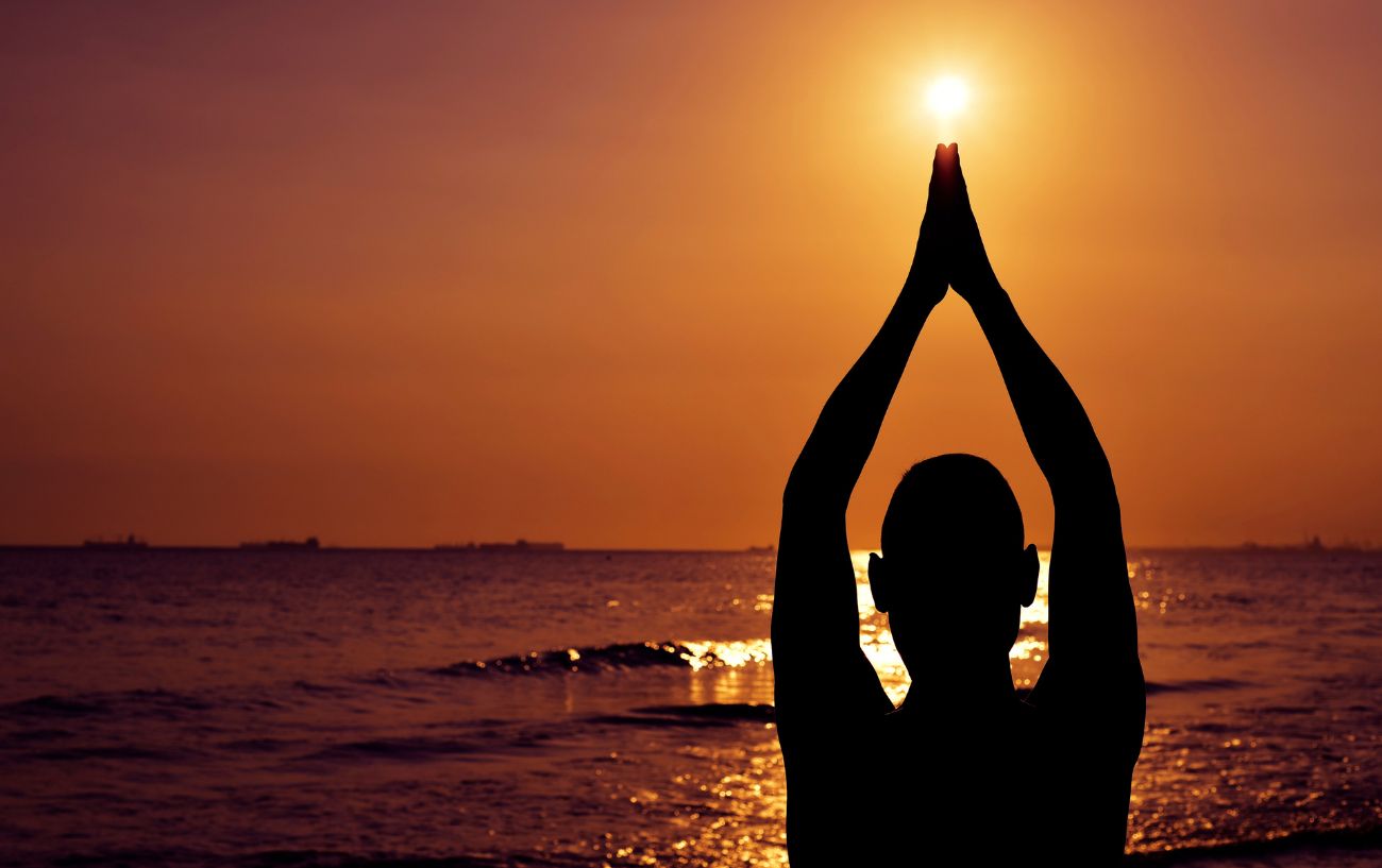 a man in front of sunrise over the beach holding his hands in prayer