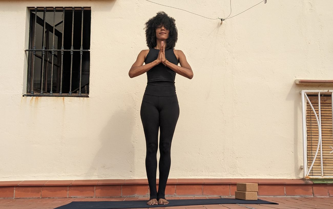 a woman wearing black yoga clothes doing mountain pose on a sunny terrace