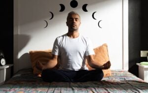 a man sitting cross legged on a bed with a moon illustration over his head