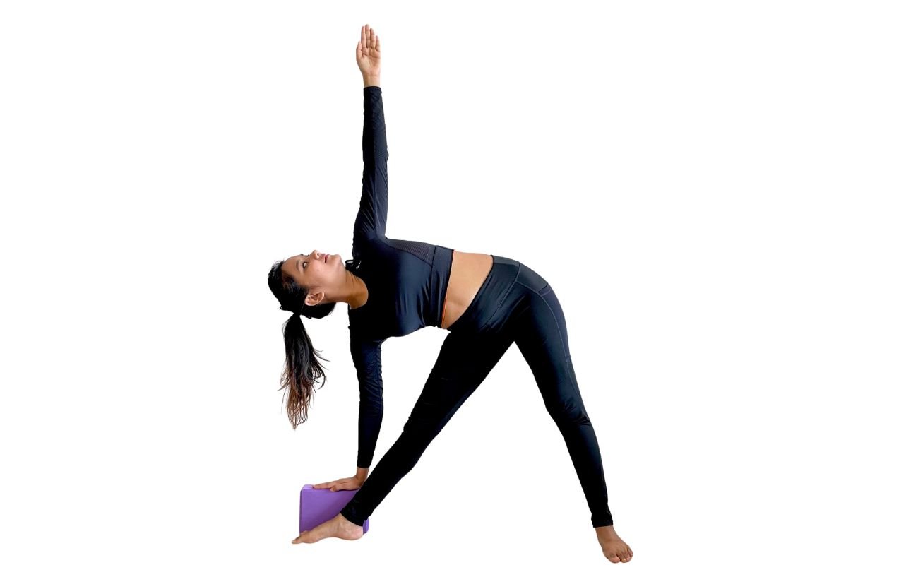 a woman wearing black yoga clothes doing triangle pose with a hand on a purple block