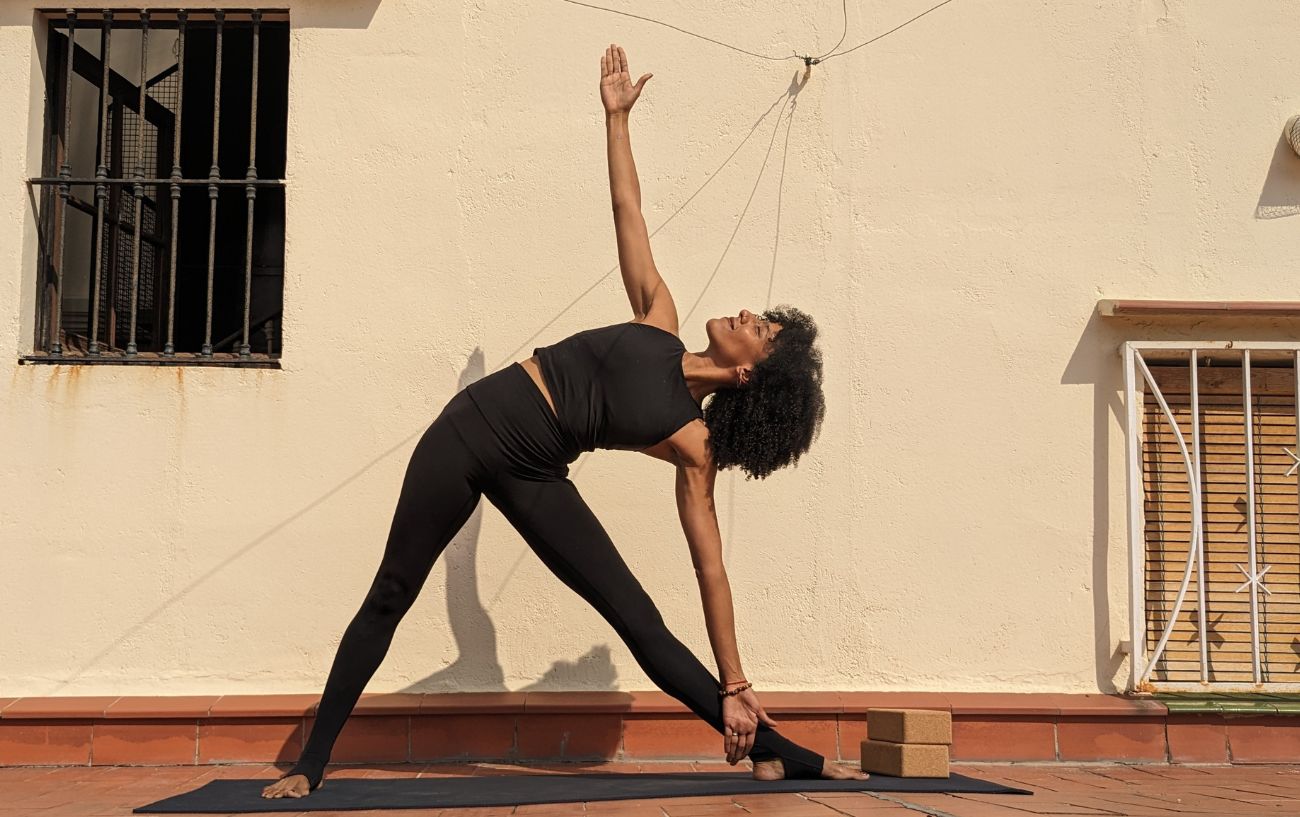 a woman wearing black yoga clothes doing triangle pose on a sunny terrace