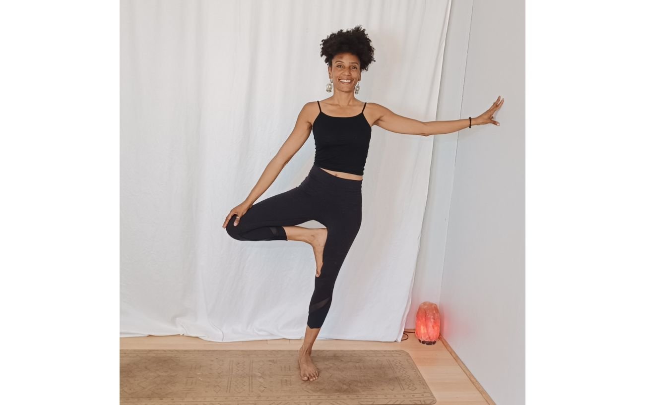 a woman doing a tree pose variation by holding a wall against a white background