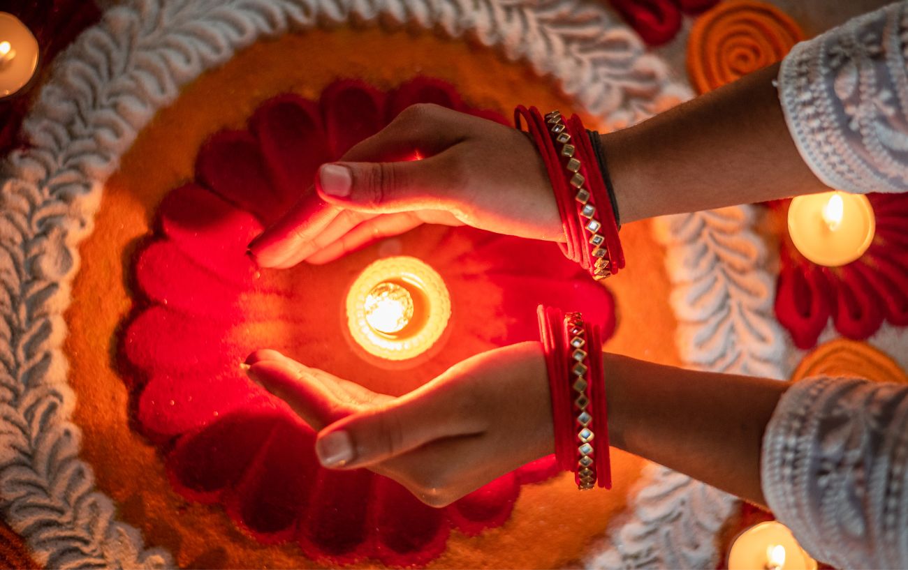 Hands cupping a candle over a puja offering. 