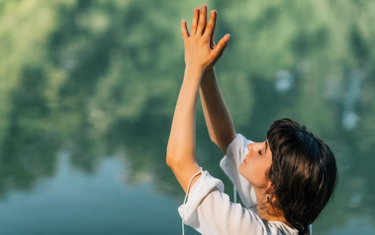 a woman in nature with hands in prayer stretched above her