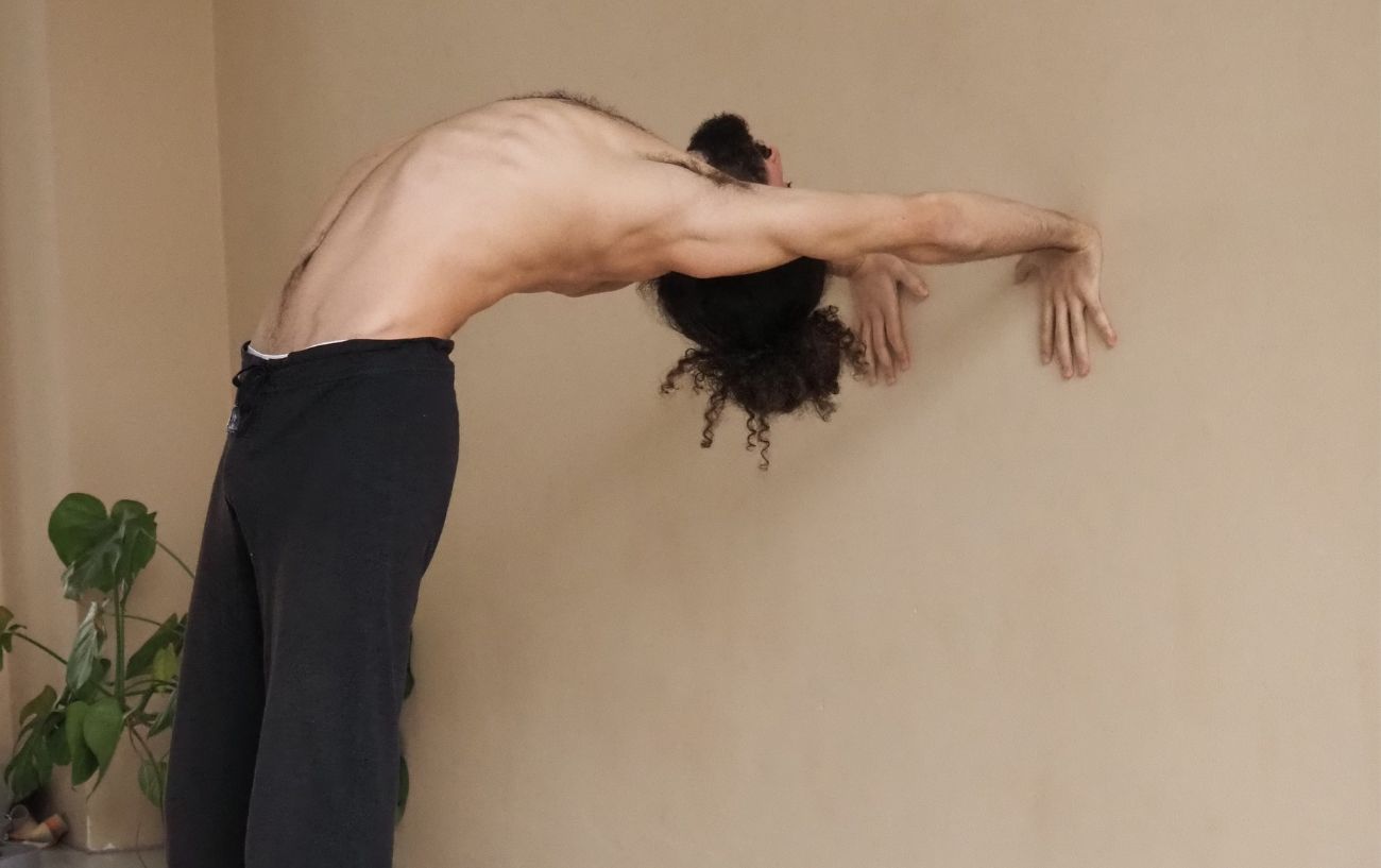 a man wearing black yoga clothes in wheel pose with his hands on a wall