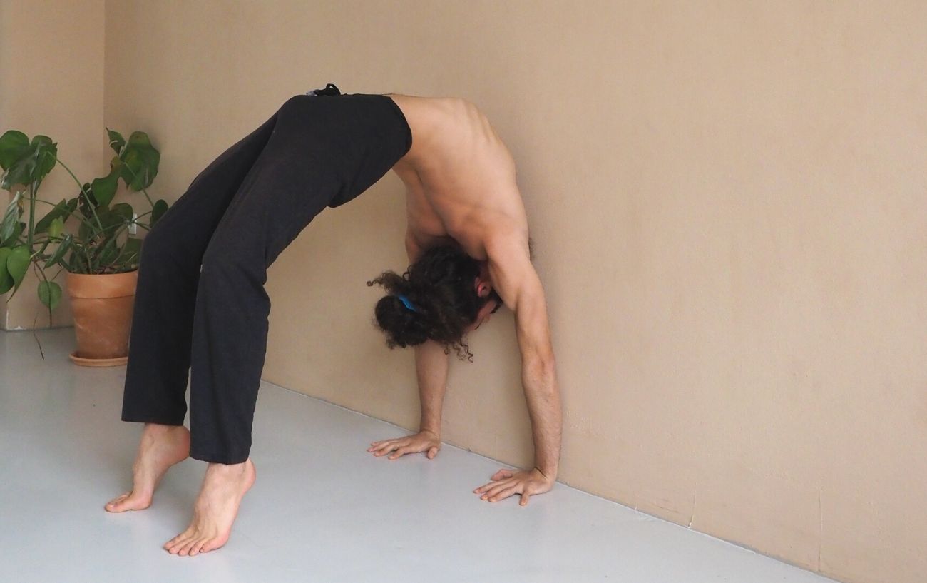 a man wearing black yoga clothes in wheel pose against the wall