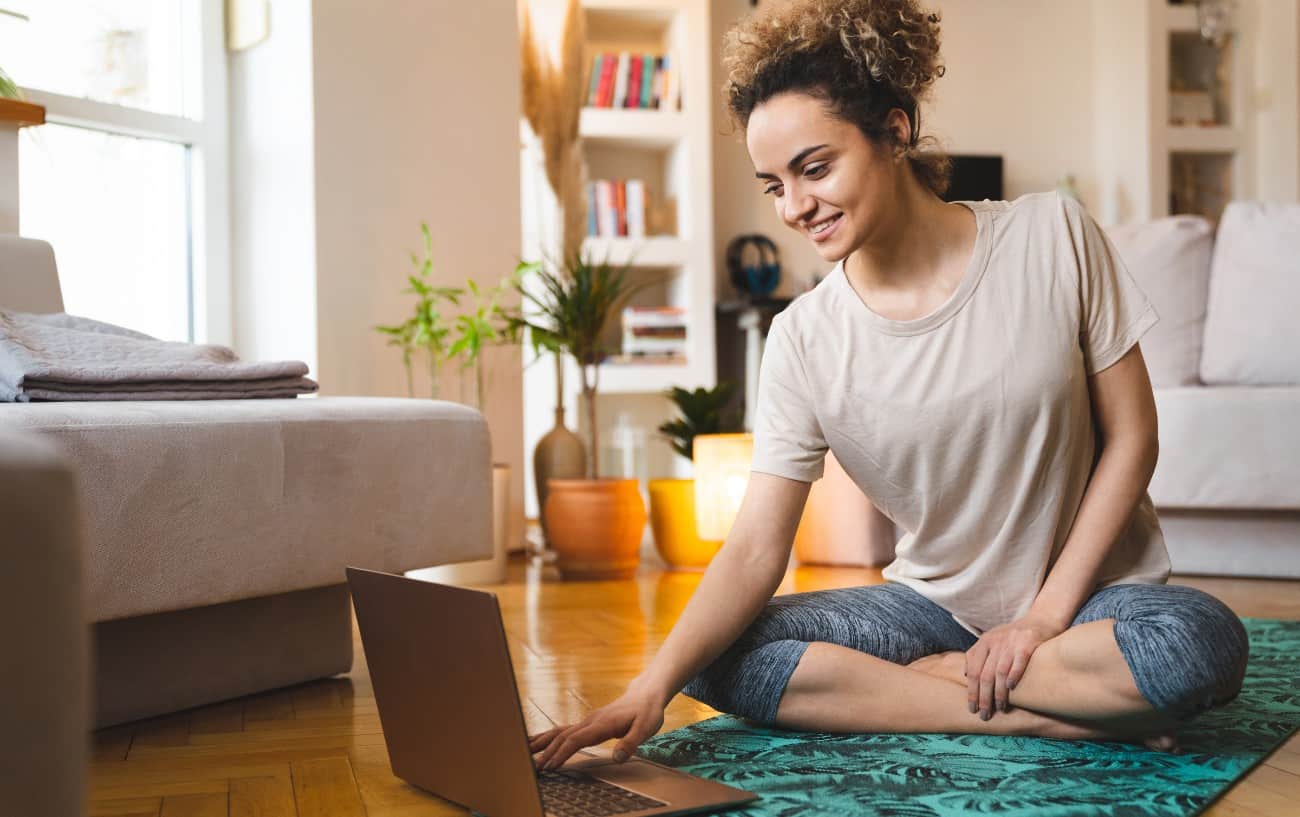 woman prepares for a yoga routine in her living room on her laptop