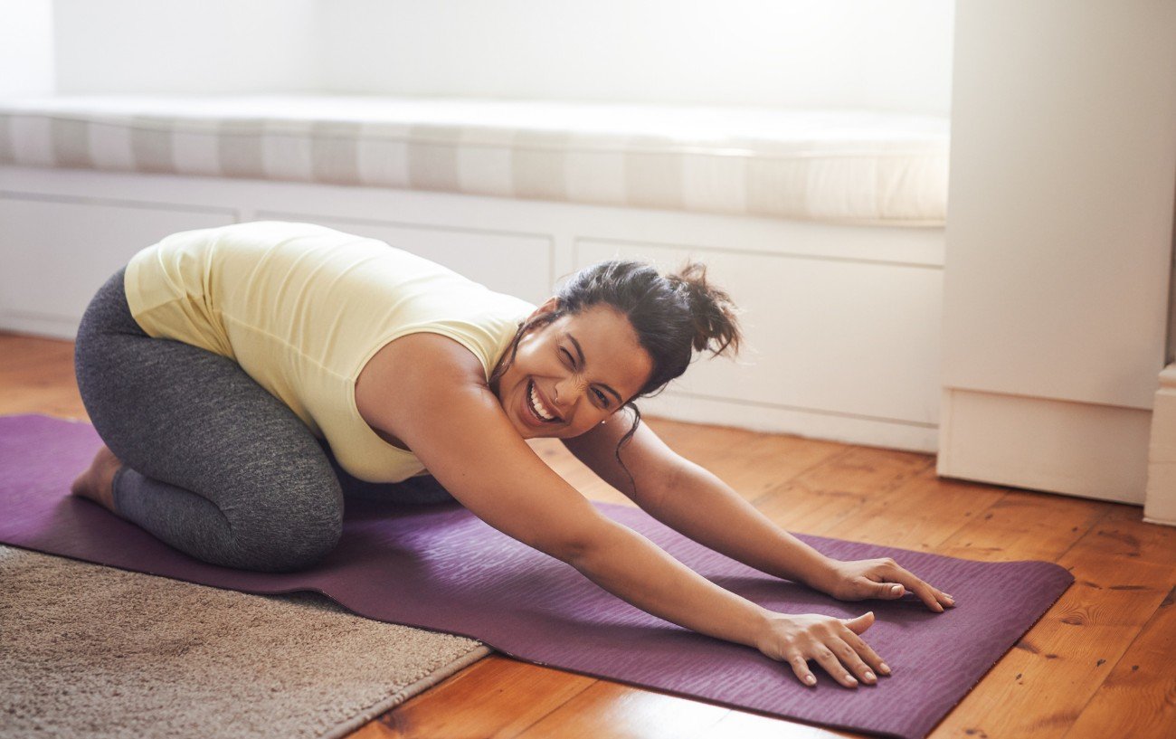 a woman laughing whilst doing a yoga pose on a purple yoga mat