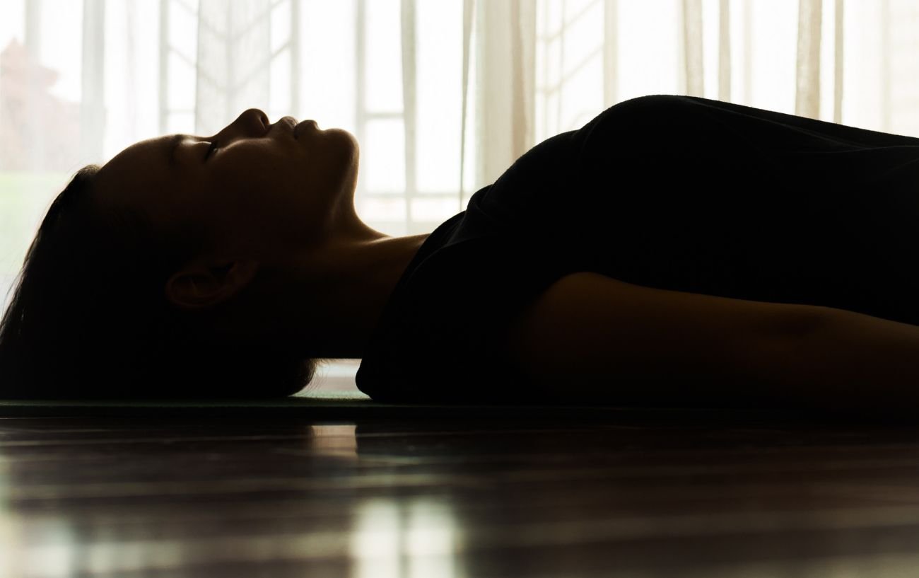 a dark image of a woman lying down in savasana