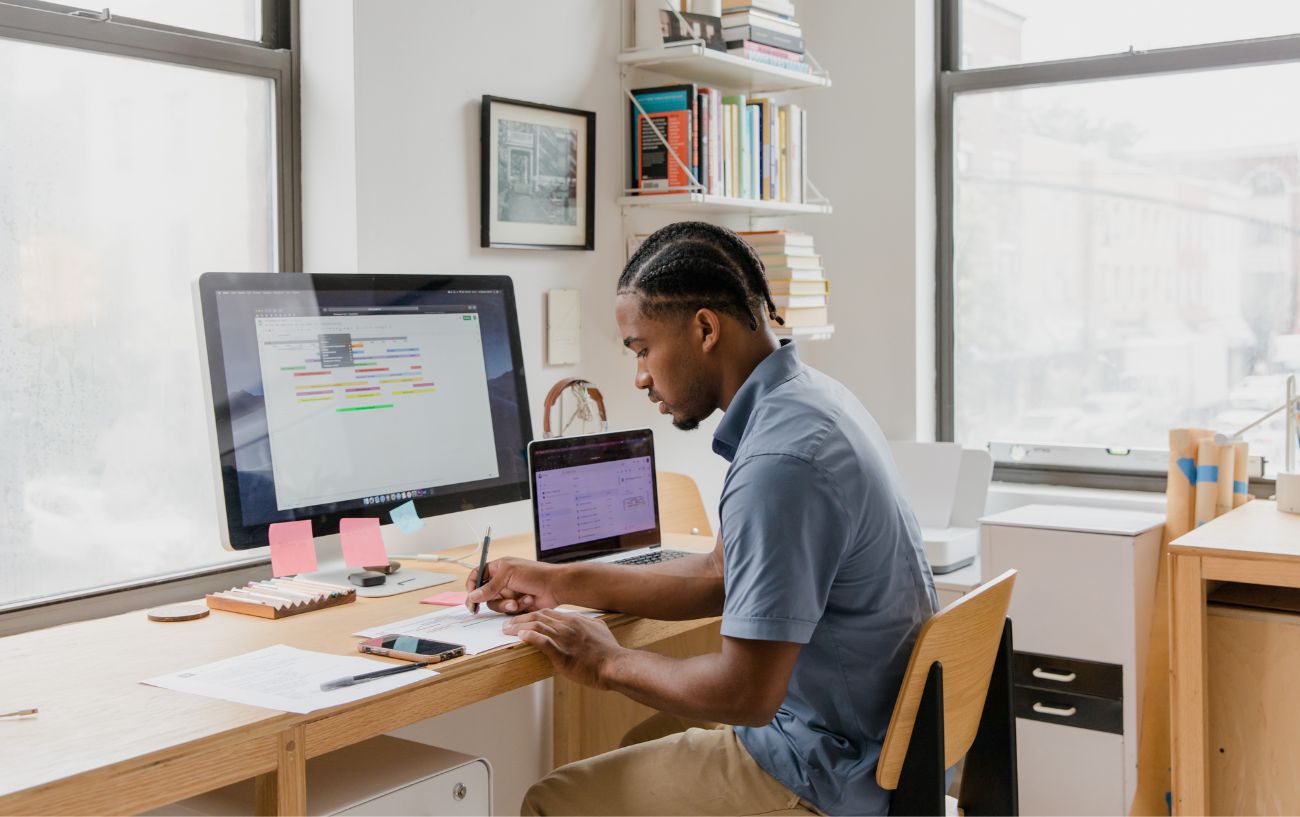 a man sitting at his desk in front of computers writing on a piece of paper