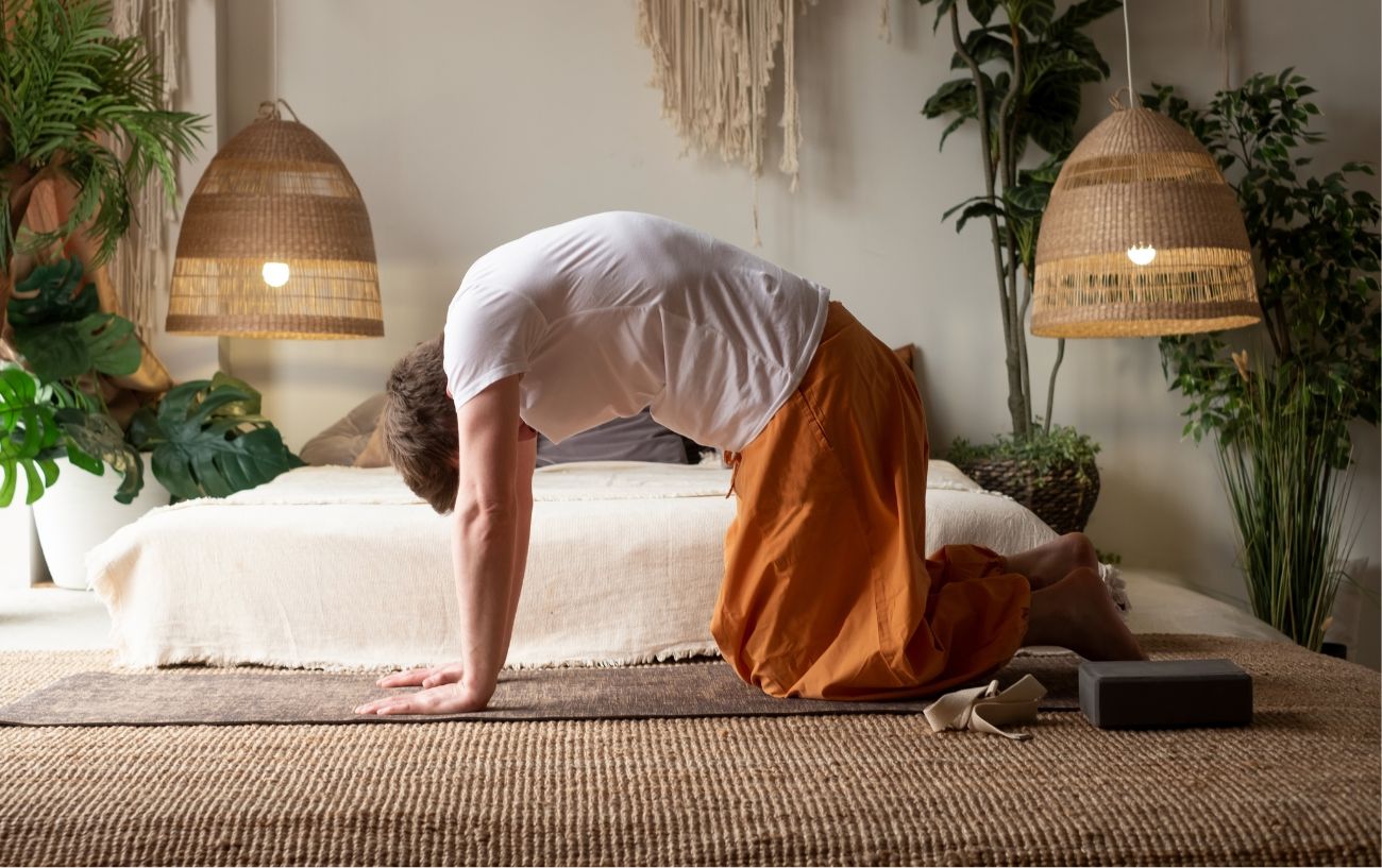 a man doing cat pose in baggy clothes in his bedroom full of plants