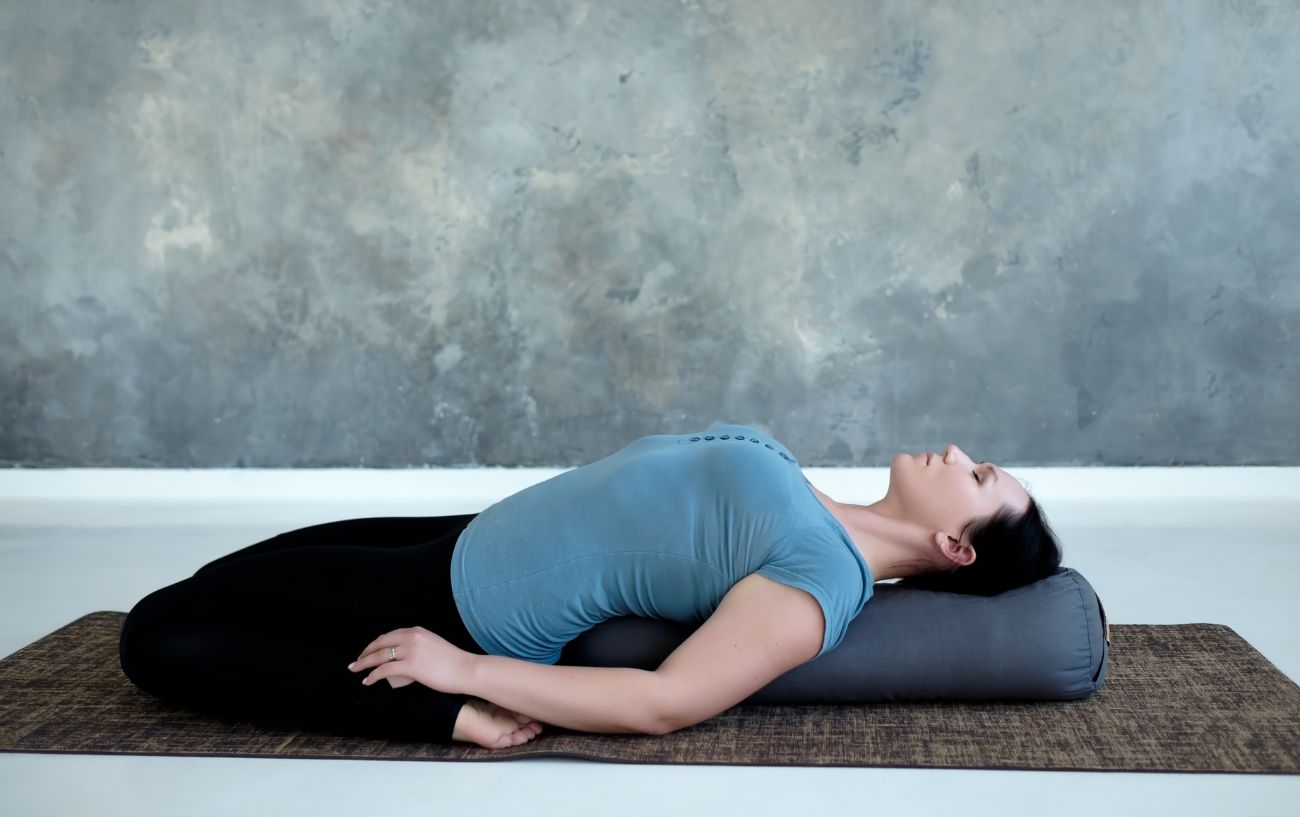 a woman doing reclined hero pose on a bolster