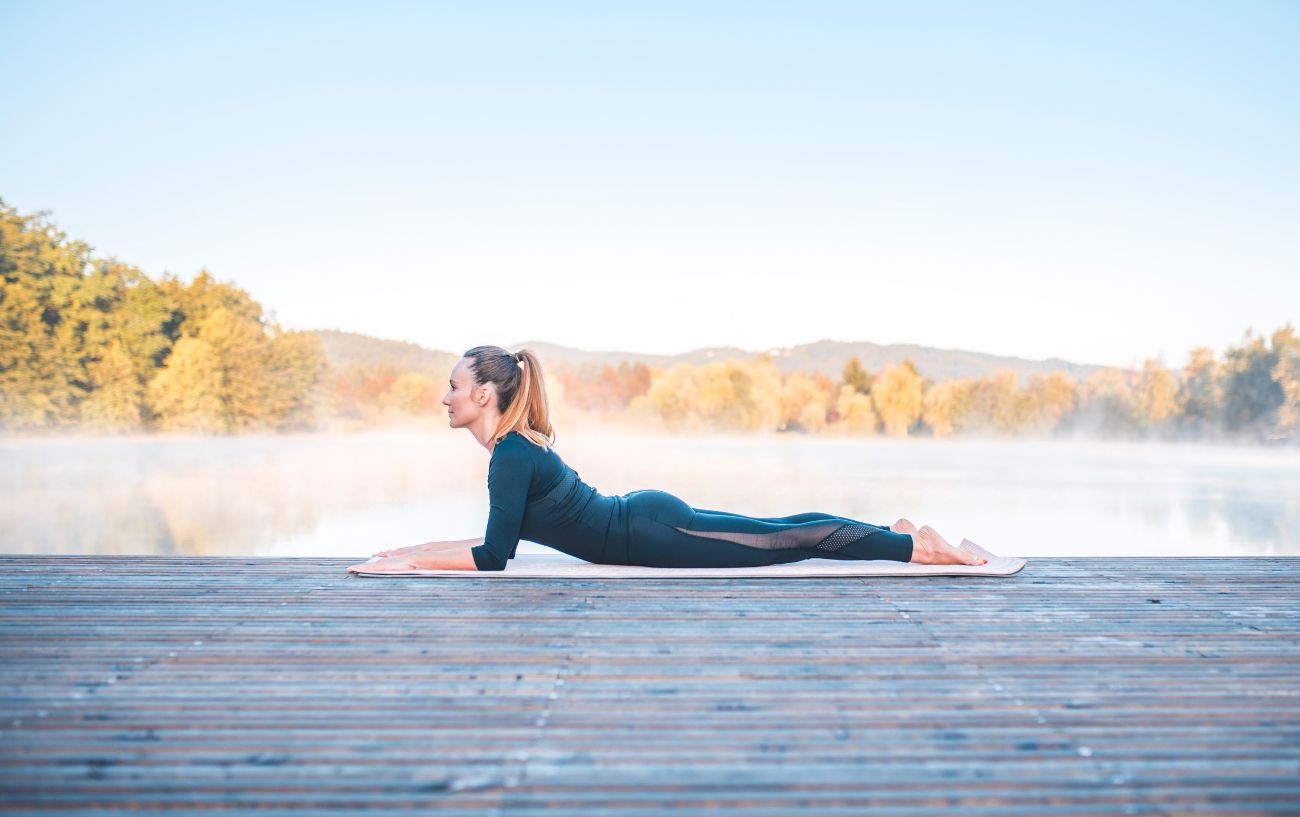 a woman doing sphinx pose on a decking in front of a lake