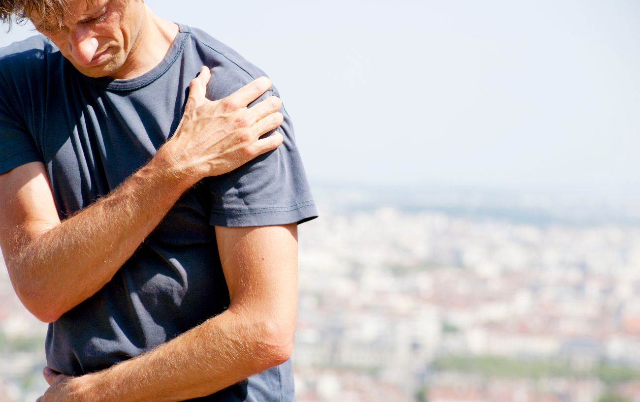 a man in a black t shirt clasping his shoulder in pain