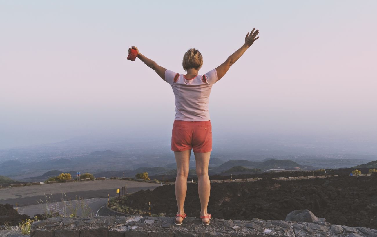 A woman standing on a hill with her arms up.