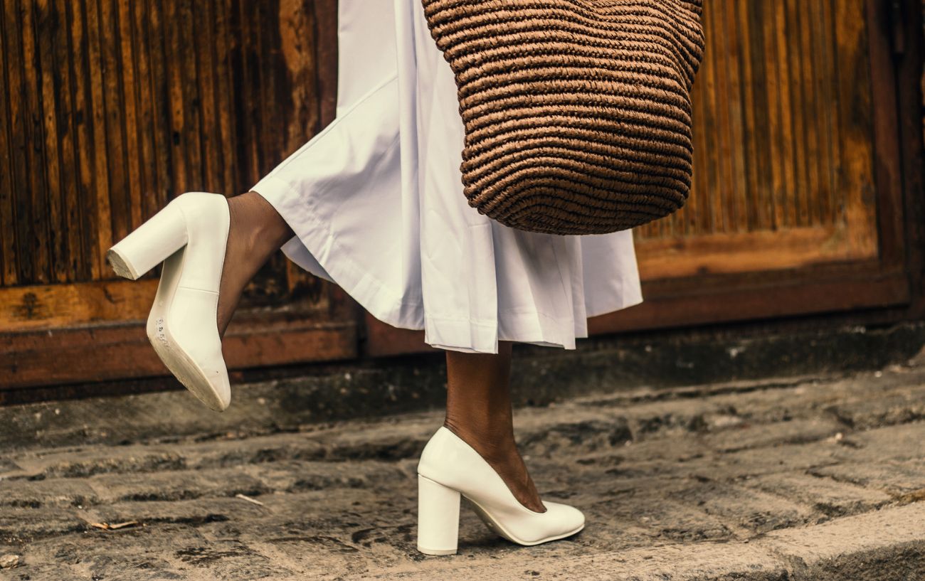 a woman walking down the road wearing white high heels and a dress