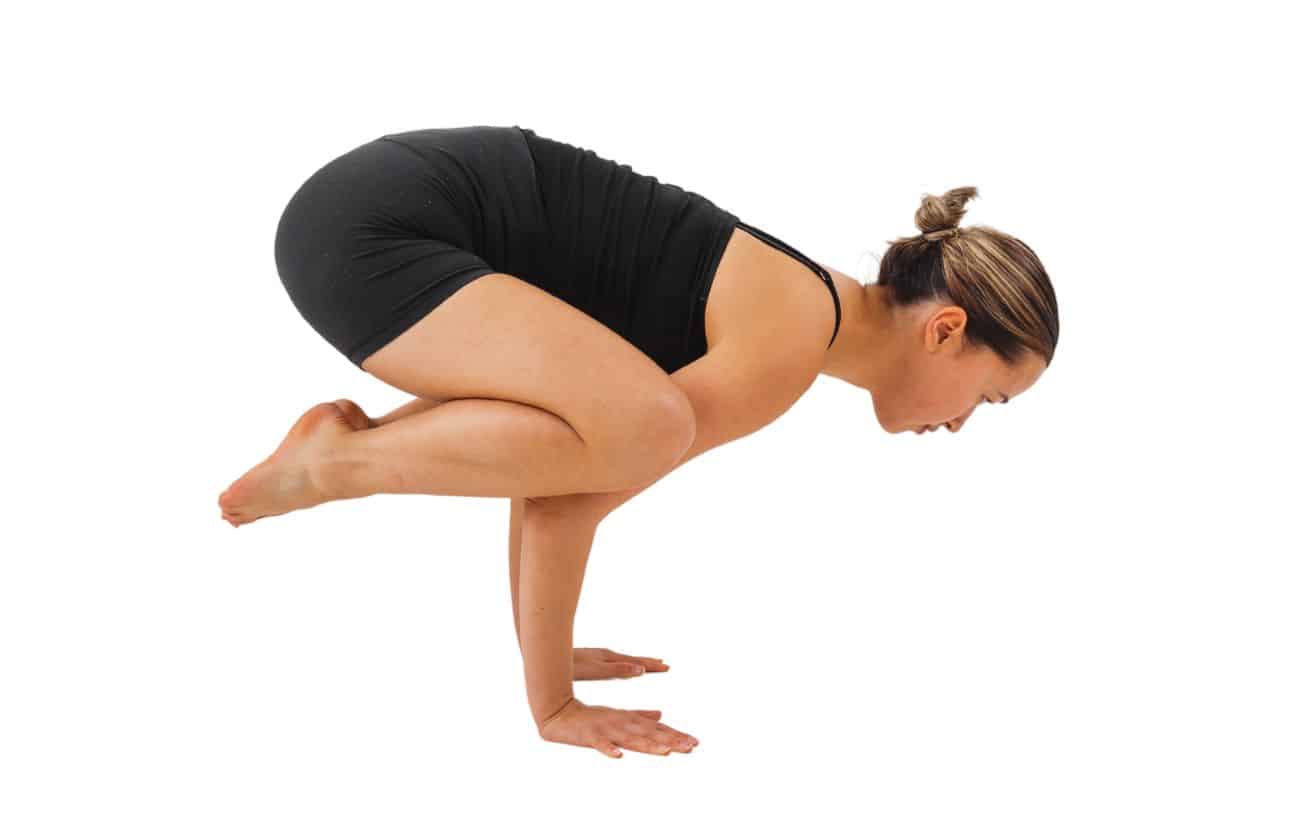 a woman wearing black yoga clothes doing crow pose, also known as crane pose